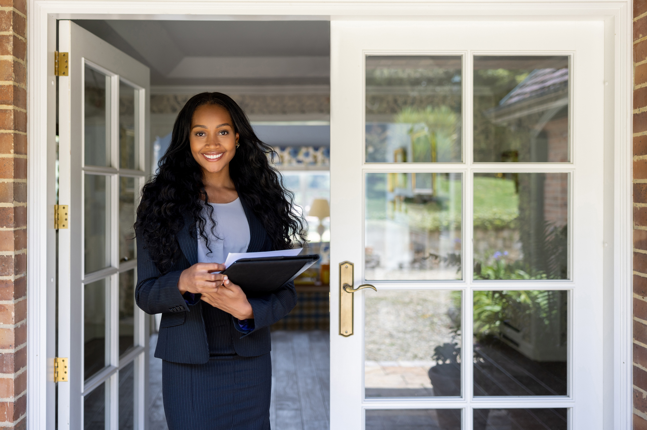 Portrait of an African American real estate agent at the door of a house for sale and looking at the camera smiling